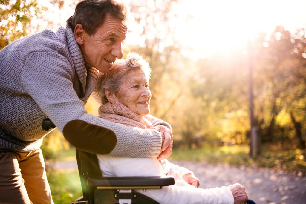 Man with elderly mother in wheelchair smiling behind her