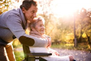 Man with elderly mother in wheelchair smiling behind her
