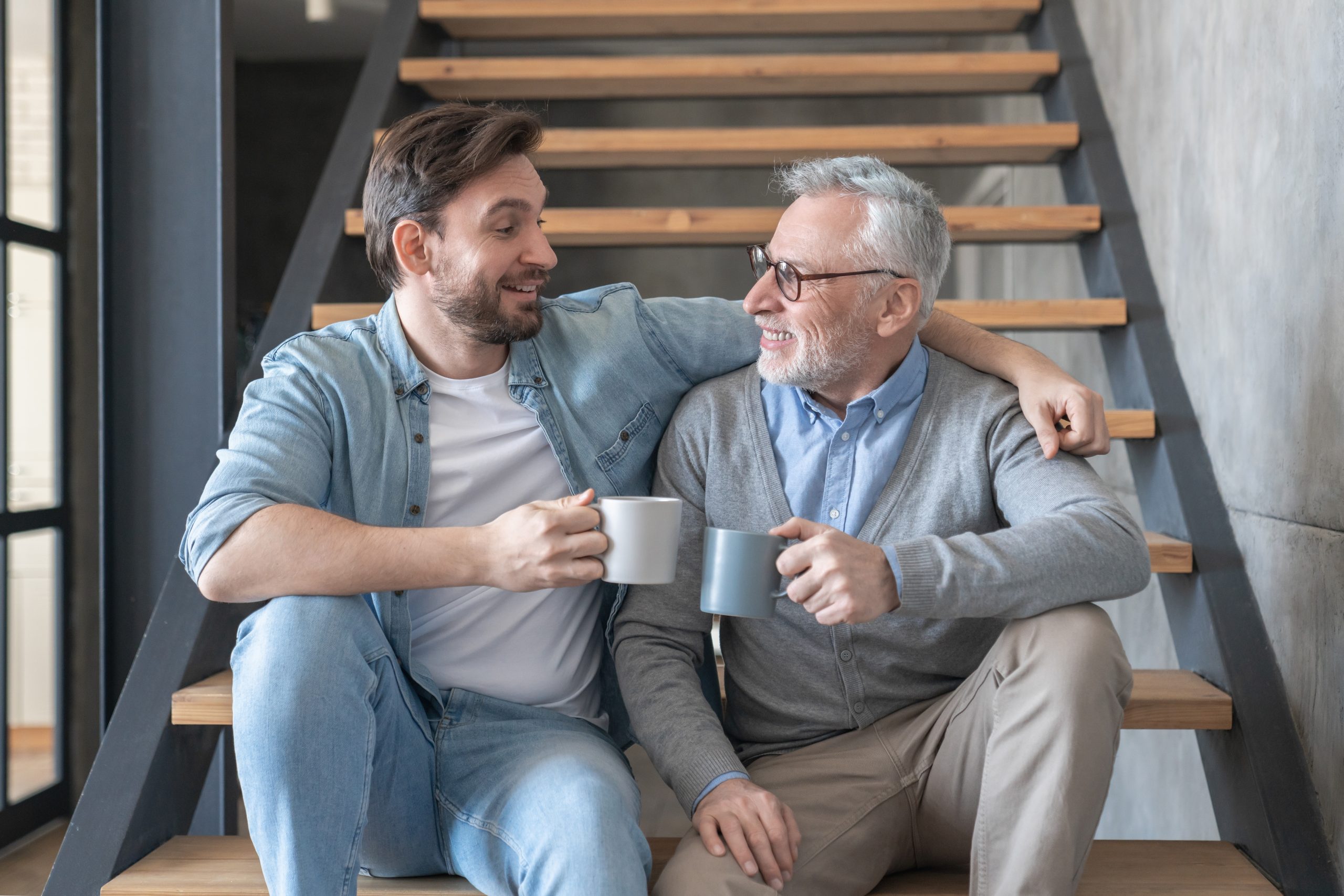 Son and Father sitting down smiling at each-other with a cup of tea each