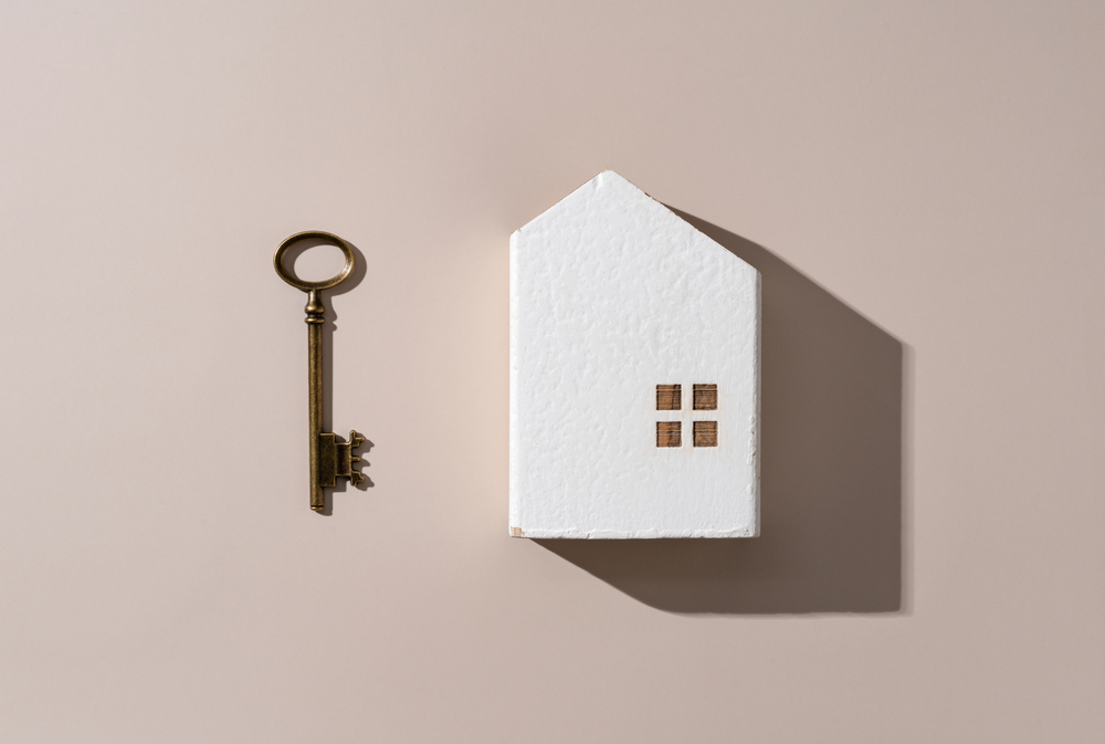 Model Of A House With Brass Keys flatlayed On A pink background