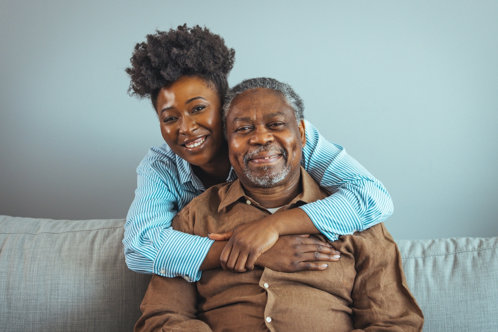 Smiling Young Woman Sitting On Sofa With Happy Older Retired Man