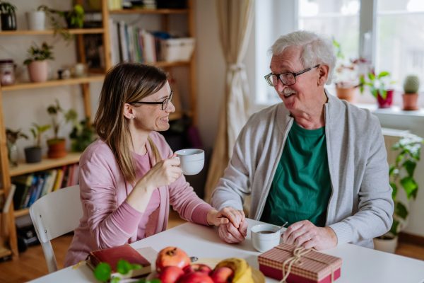 Elderly Father and adult daughter holding hands over a cup of coffee