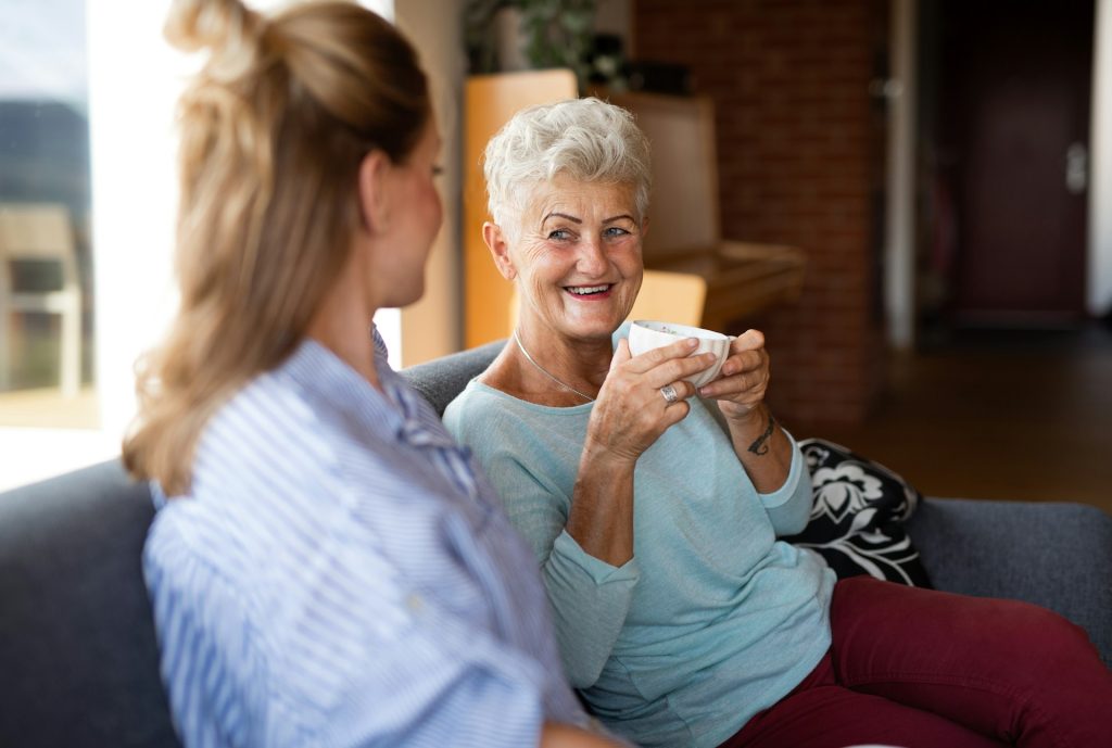 mother holding a cup of tea and smiling to her adult daughter